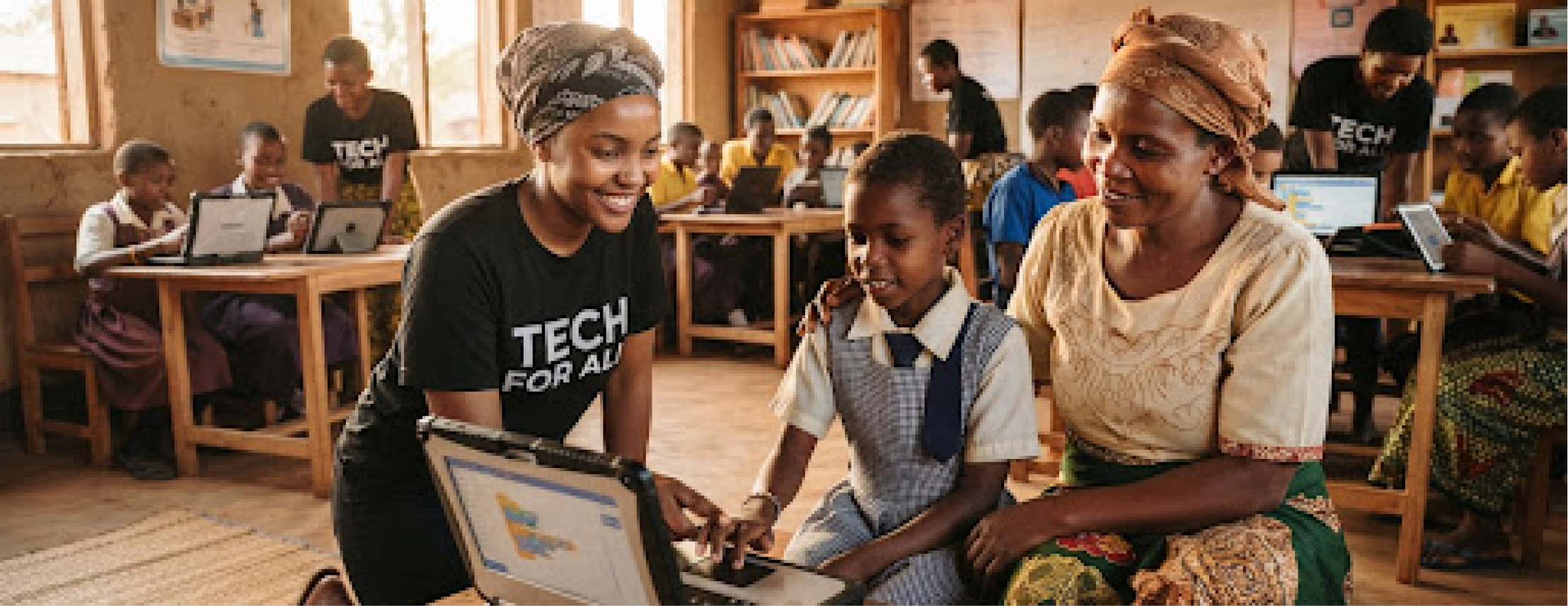 A volunteer helping a mother and child with a laptop at a community learning session